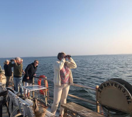 Bezoekers kijken met een verrekijker over de Oosterschelde tijdens de boottocht